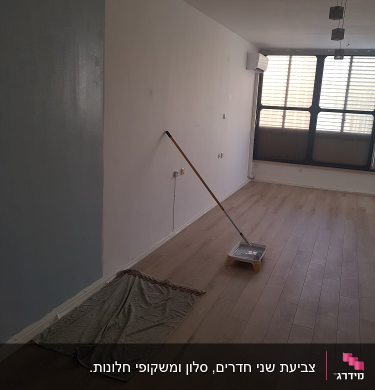 קיר צבוע חלקית, מגש צבע ומברשת על הרצפה
